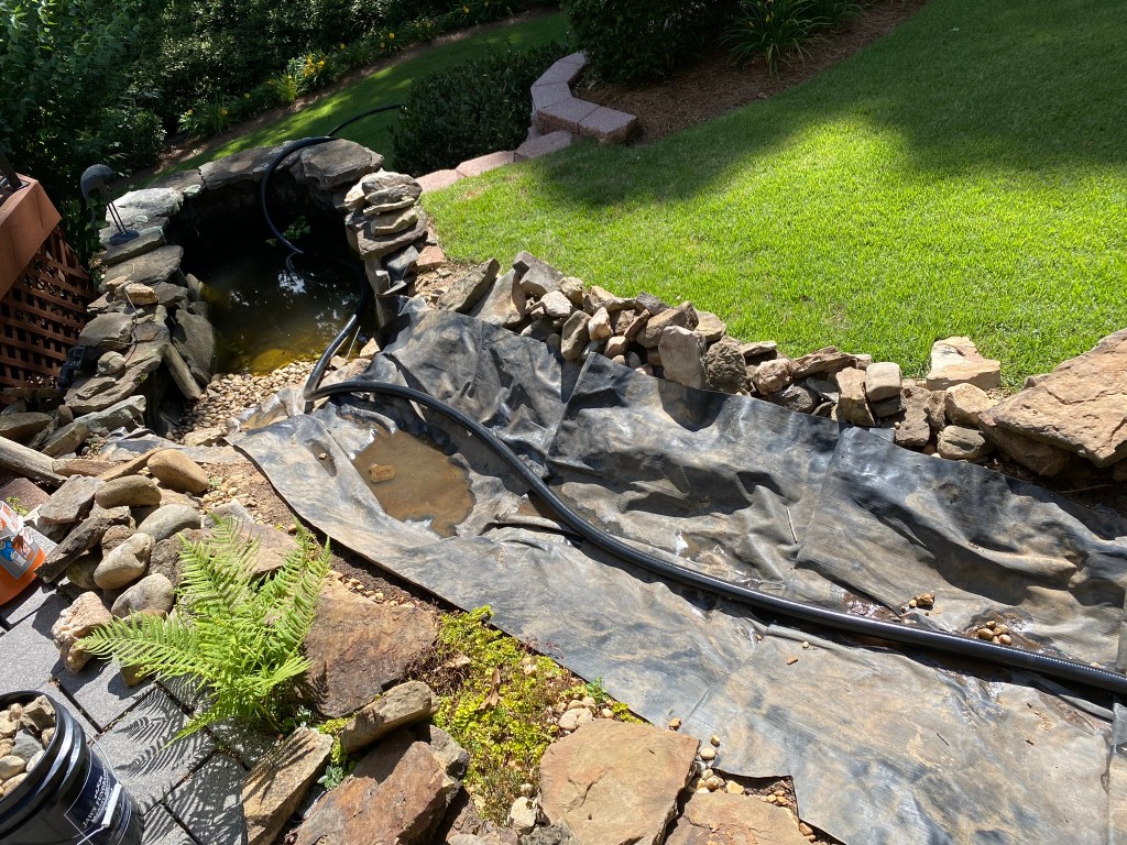 Backyard stream bed with rocks removed revealing feed line and liner