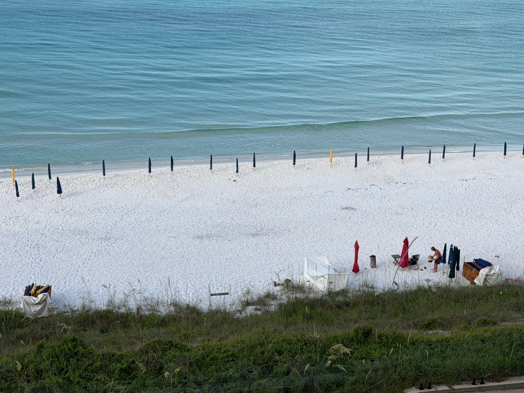 A line of wrapped beach umbrellas in a row on a white sand beach with emerald green waves lapping at the shoreline
