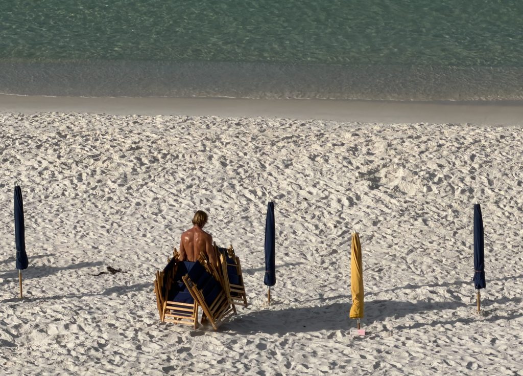 A young man carrying a dozen beach chairs across a beach