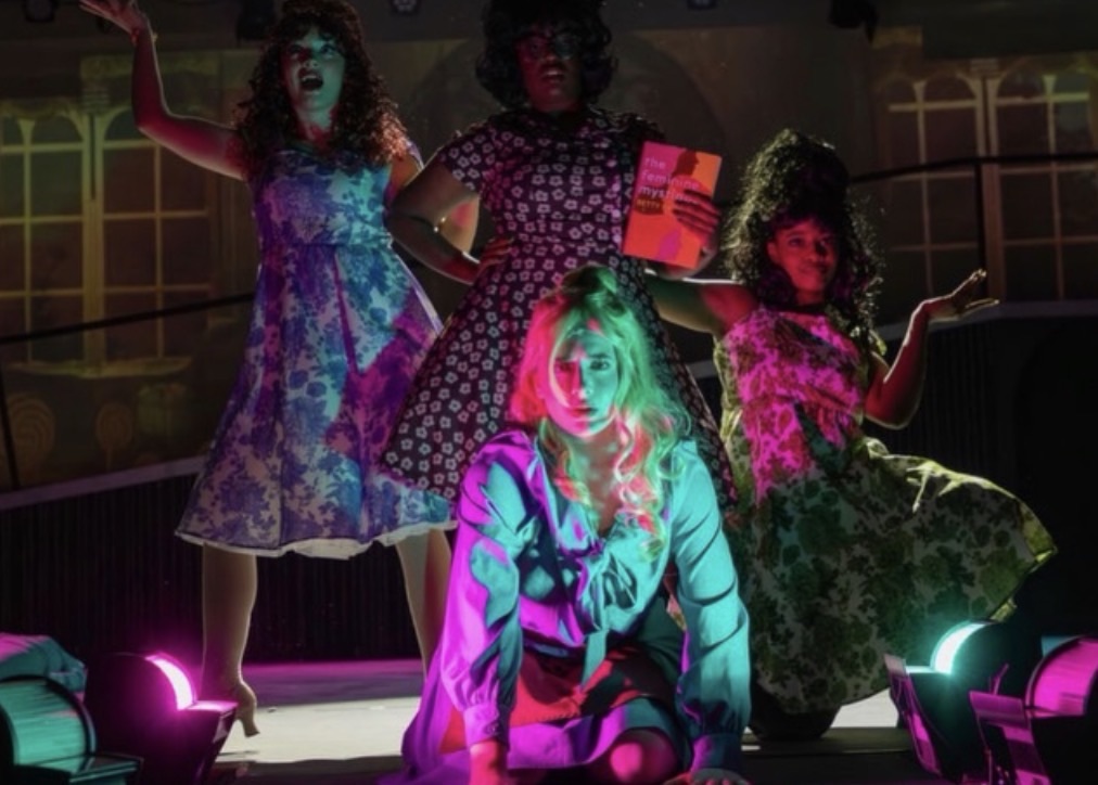 Cinderella surrounded by her stepmother and stepsisters on stage with green and pink lights