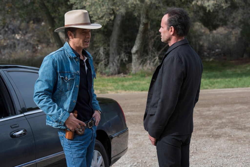 A man in denim jacket and cowboy hat talks with a man in a black jacket
