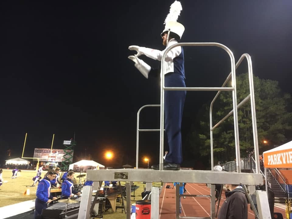 A drum major conducting the band from a metal platform
