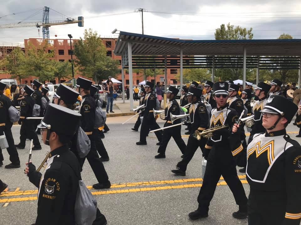 A college marching band marches in formation down a street.