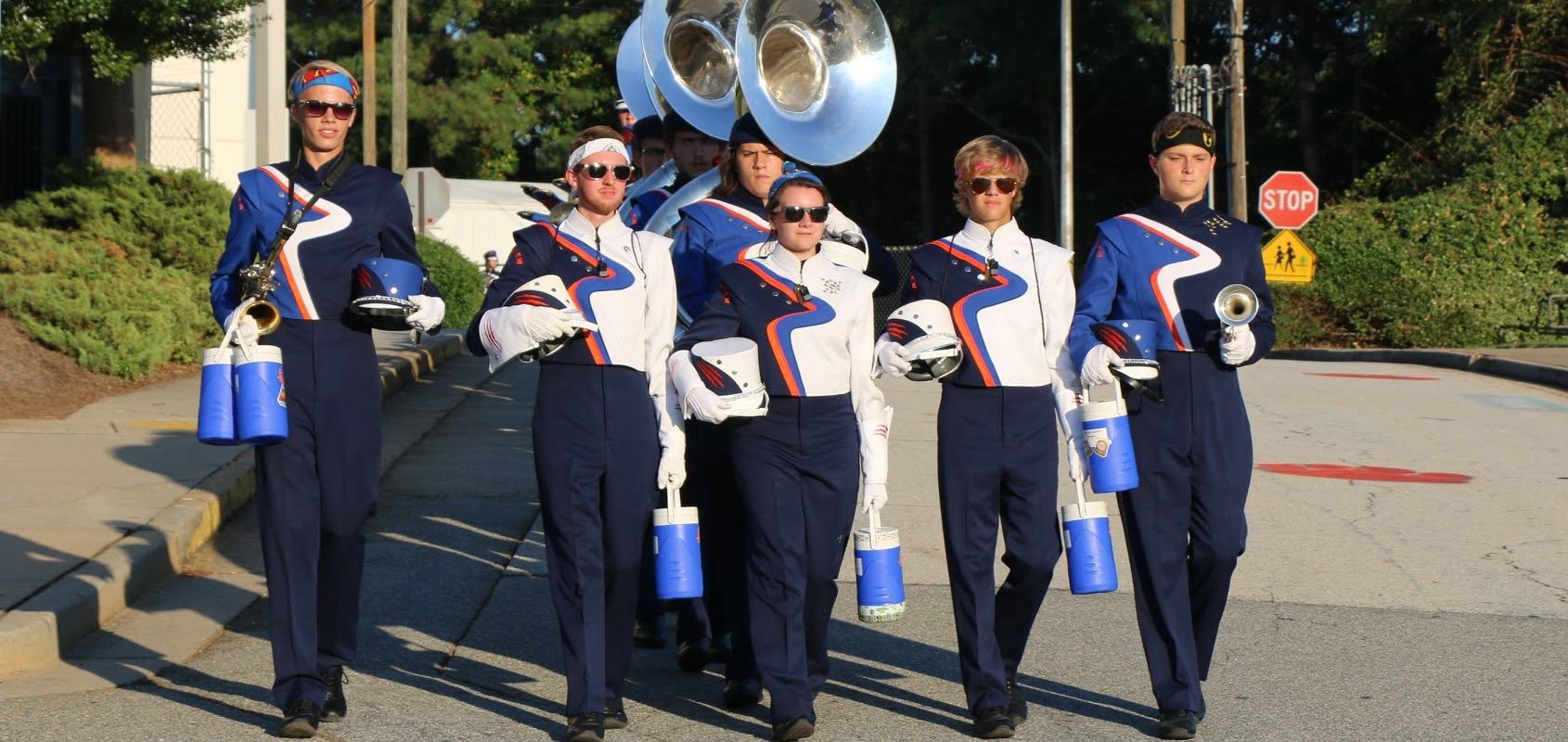 Drum majors and band captains march down the street leading the marching band toward the stadium.