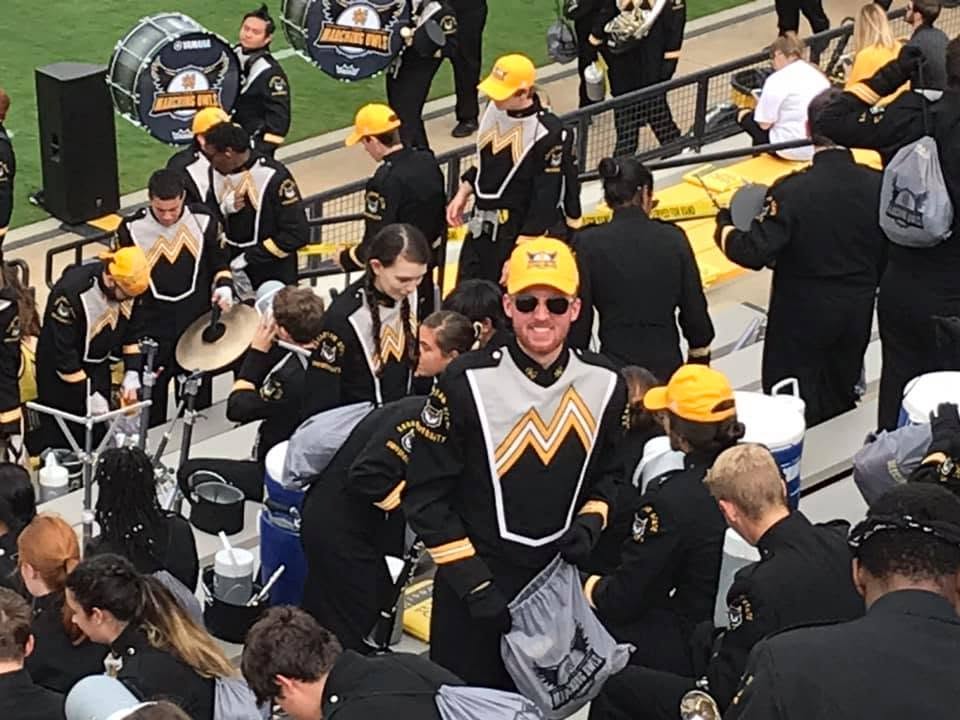 A young man in band uniform in the stands at a college football game