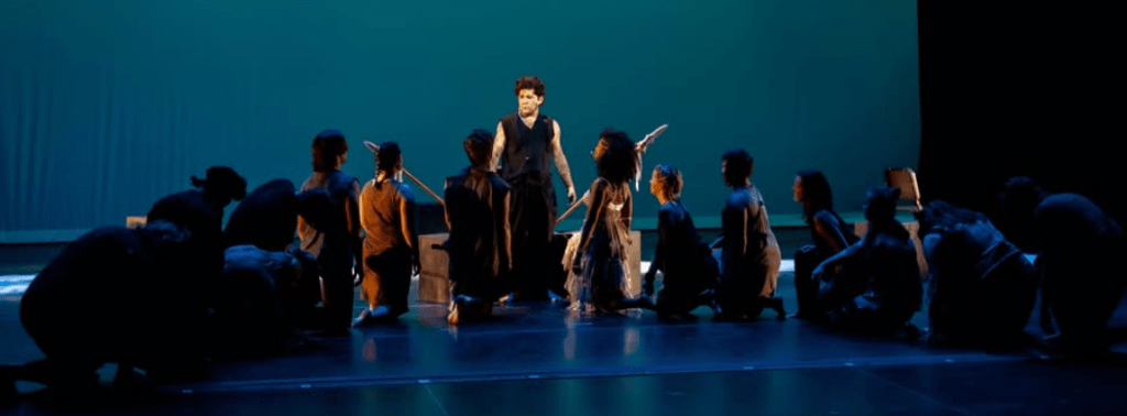 A man stands among a group of actors in costumes