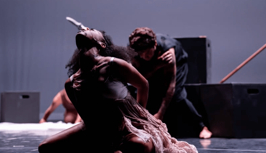 A woman writhes on a stage with a man in the background
