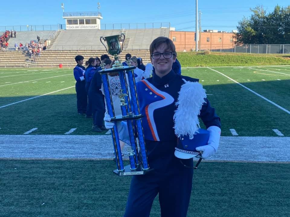 A marching band member holds a giant trophy