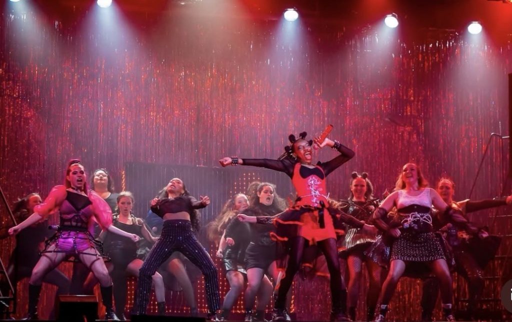 Teenage girls sing on a stage with red lighting
