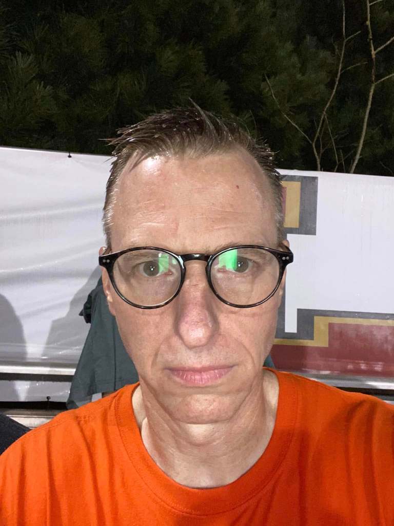 A soaking wet man in glasses