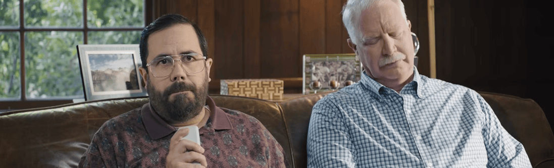 Two men sitting on a couch with one holding a TV remote