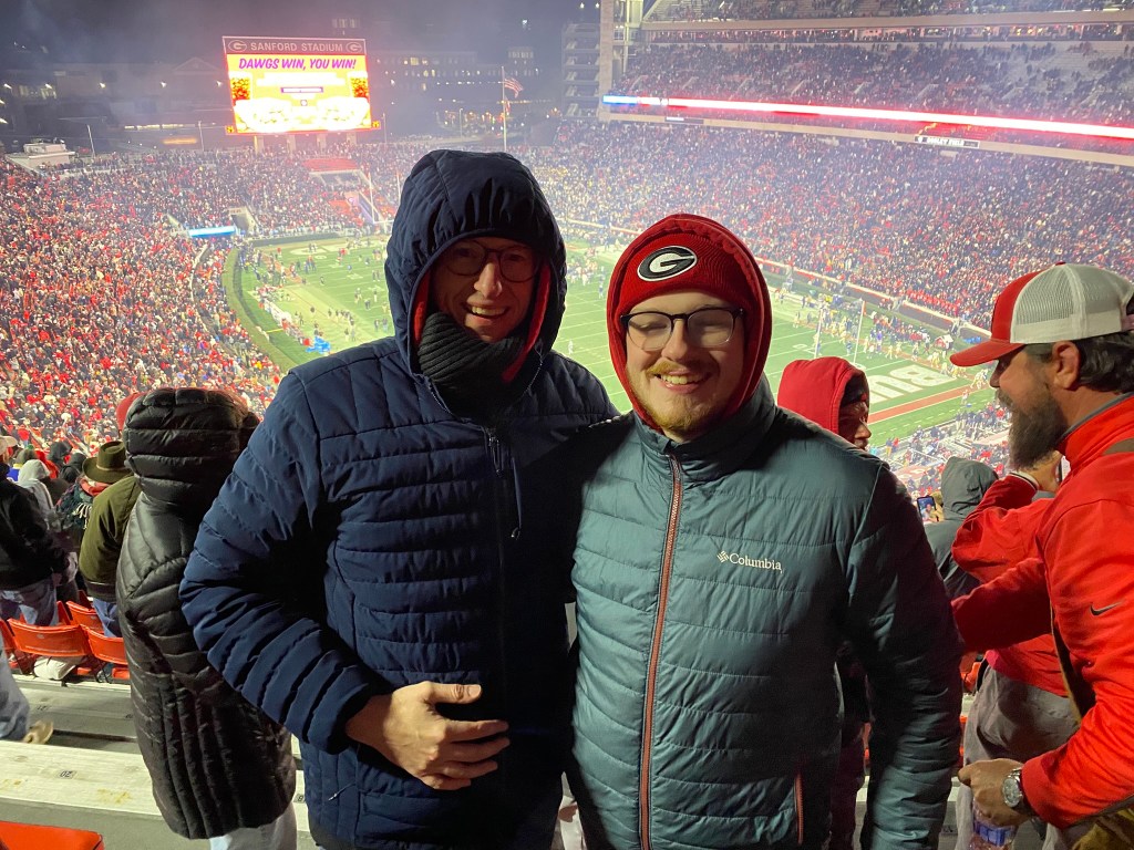 Two men in heavy coats in the upper deck of a football stadium