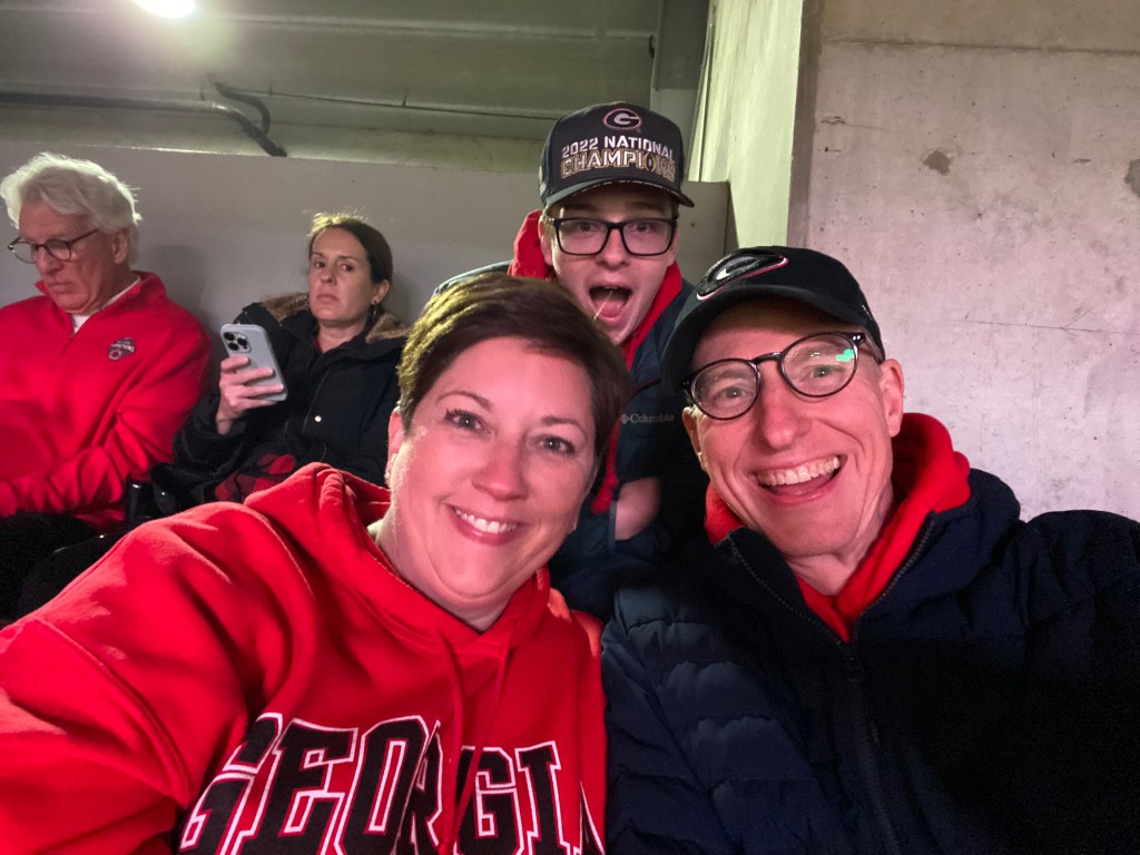 A husband and wife and adult son in University of Georgia attire at a college football game