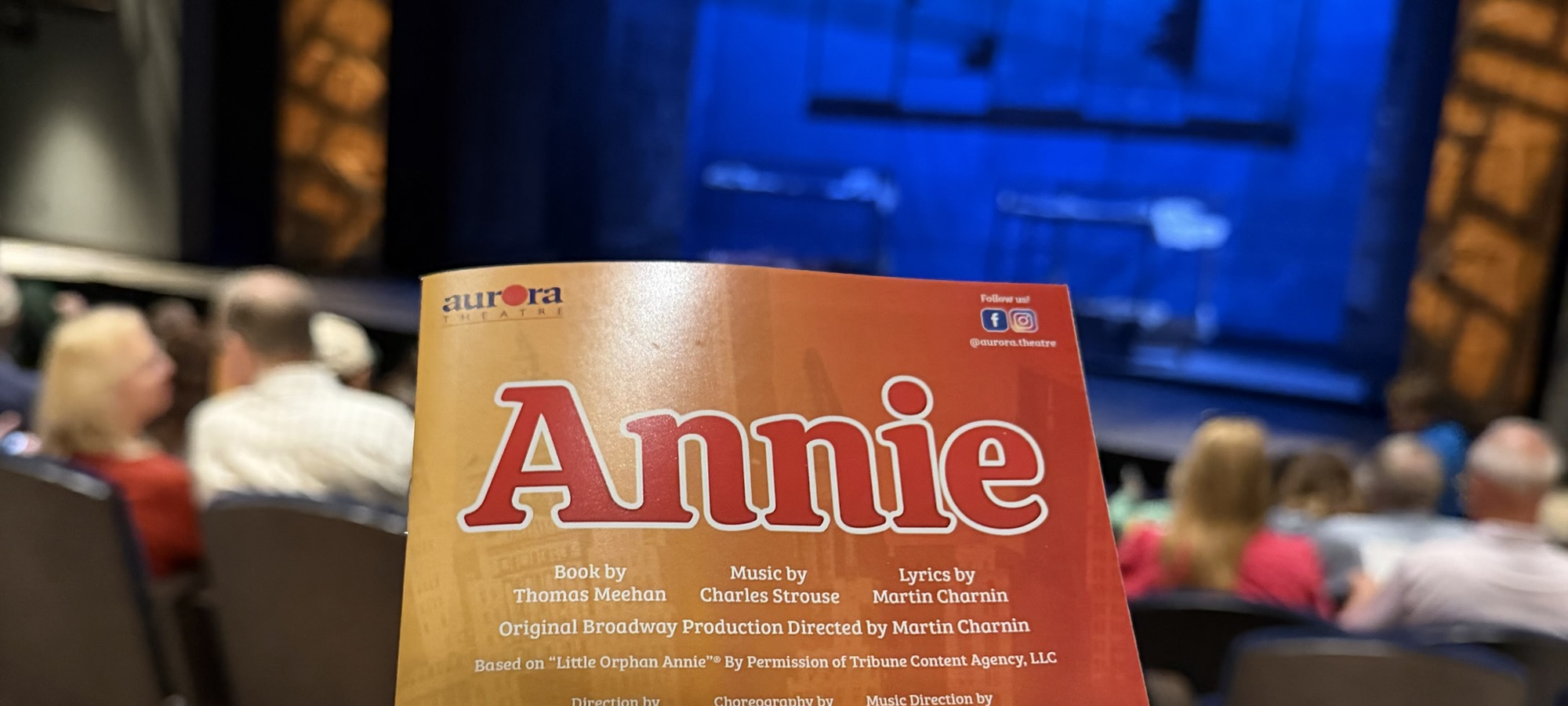 The top of a theater program for "Annie" with the stage lit in blue in the background.