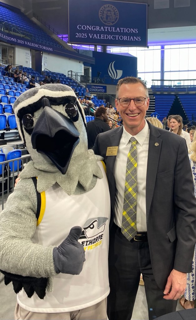 A man in a suit and tie with the Oglethorpe University mascot Petey the Petrel