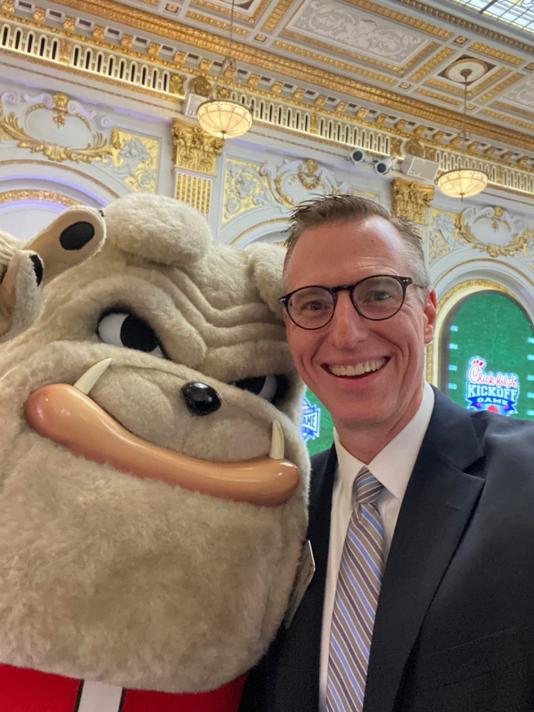A man in a suit and tie with the University of Georgia mascot Hairy Dawg