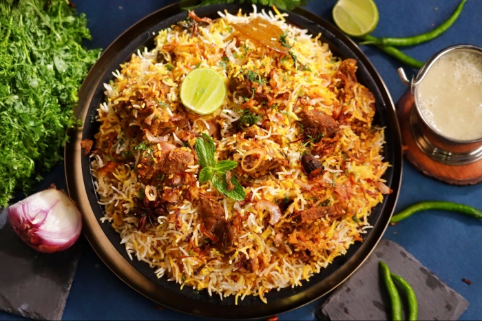 a plate of mutton biryani with spices surrounding it.