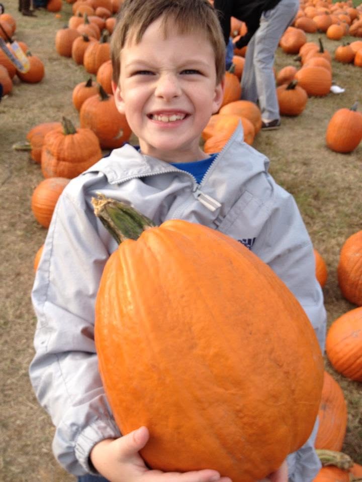 A boy grimacing while hoisting a big pumpkin