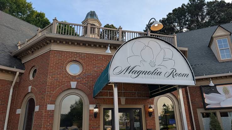 Outside of a brick restaurant with a green and white awning that says "Magnolia Room"